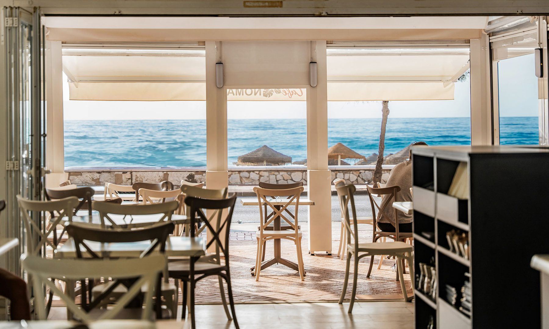 The dining room of Café Nomad, glass doors folded back onto the beach and the sea.
