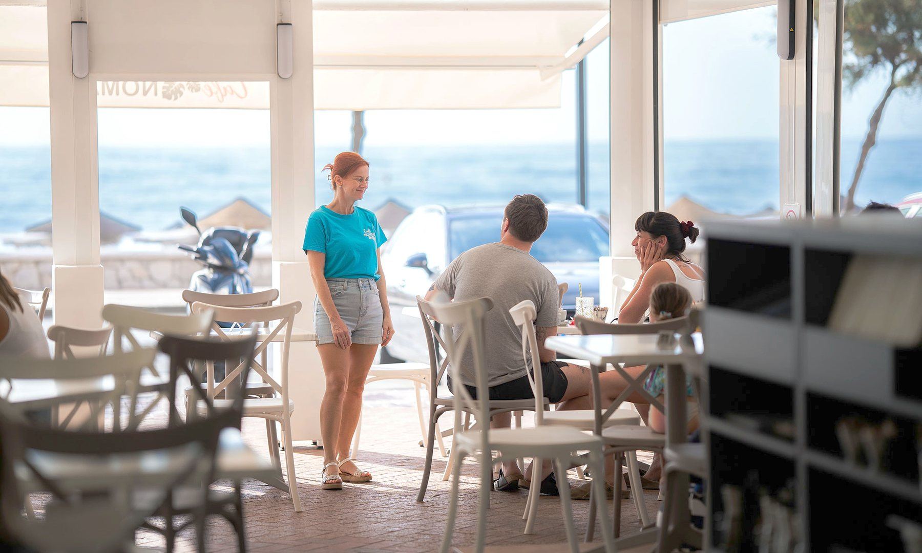 Café Nomad in service, tables facing the beach and a server crossing the room.